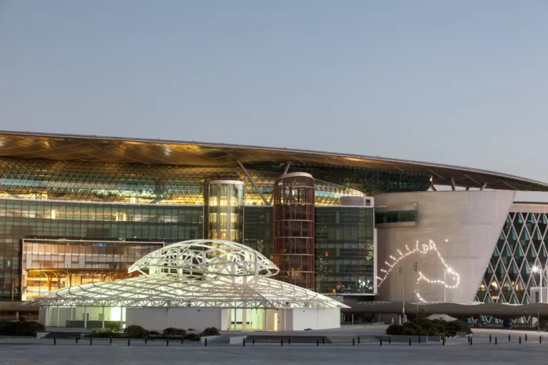 Exterior view of Meydan Racecourse in Dubai at dusk, featuring modern architecture and illuminated horse head design on the building.